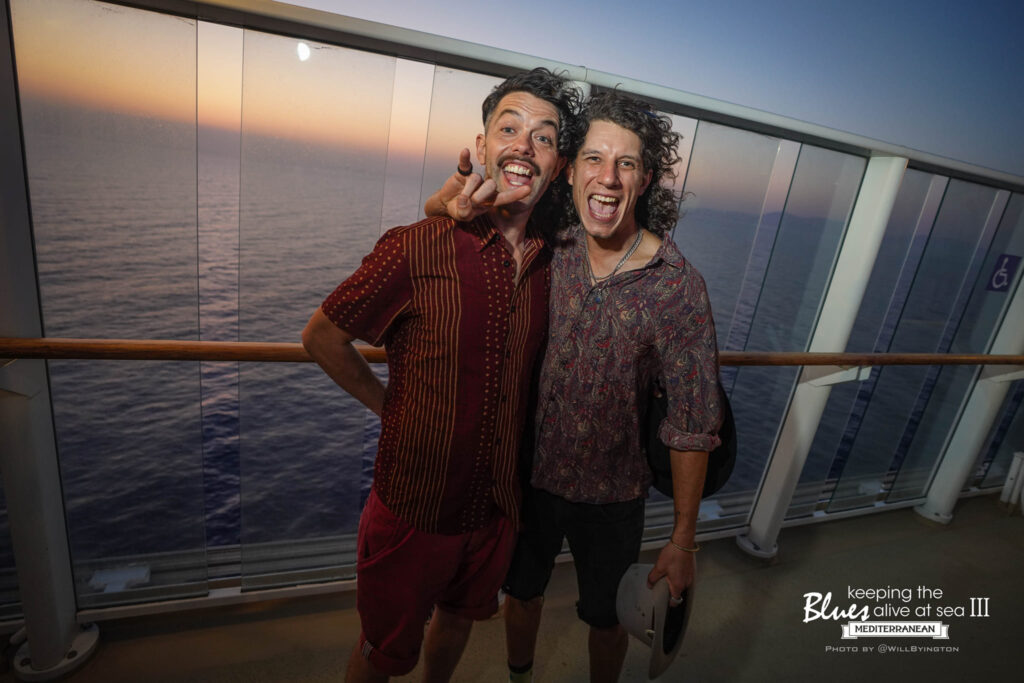 The duo pulling faces for the camera on a cruise ship deck at sunset, the Mediterranean behind them — Keeping the Blues Alive at Sea III