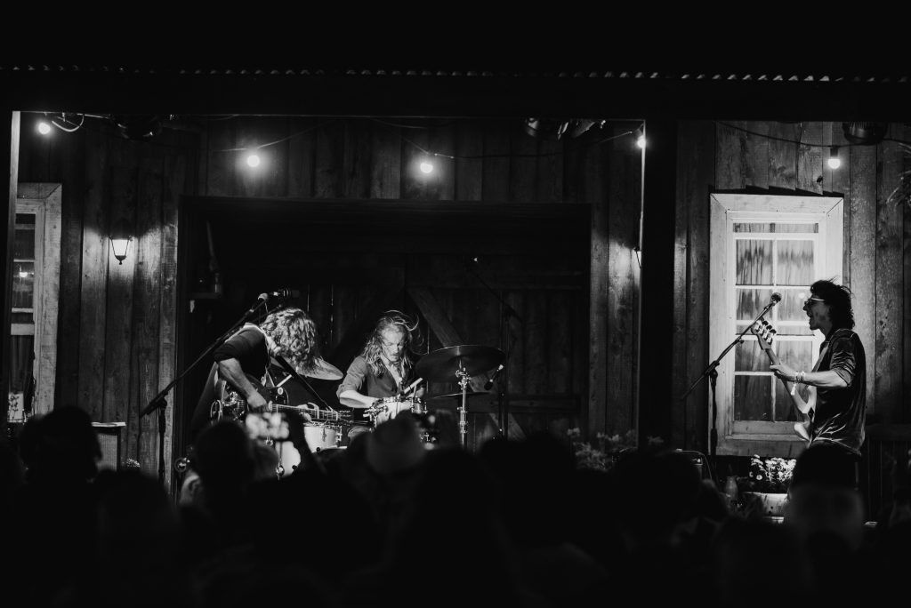 Black and white: the band playing on a wooden barn stage strung with festoon lights, the crowd silhouetted in front