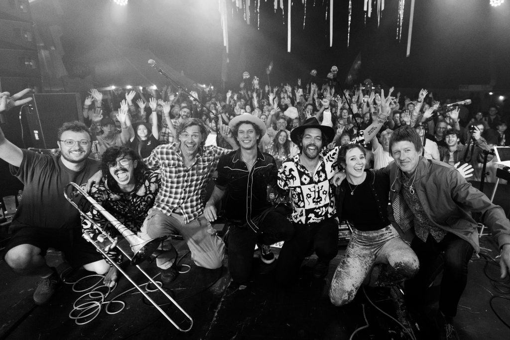Black and white: the band and their players crouched at the front of the stage for a group photo, the crowd behind with hands in the air